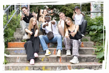 Eine gruppe junger menschen sitzt auf einer Treppe, dem Betrachter zugewandt und zeigen auf den Betrachter.